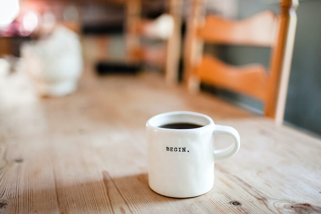 A coffee mug in a wooden table that reads - BEGIN